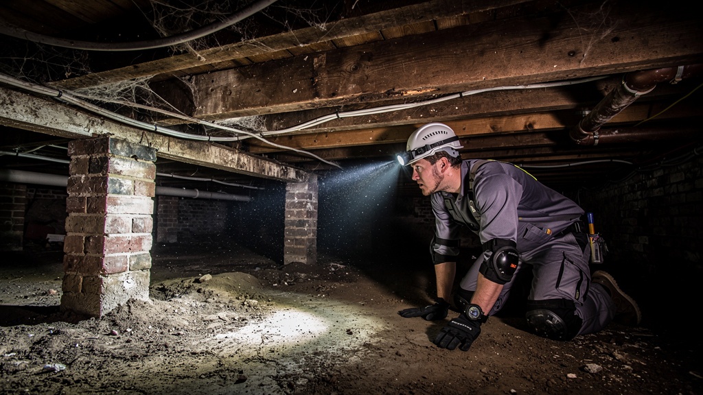 Surveyor inspecting floor joists in crawl space of old Surrey home
